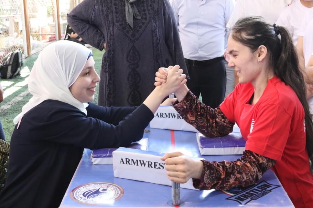 Special Advisor on International Disability Rights Sara Minkara (left) arm wrestles with a member of the Girls Environmental Club & Girls Sports Club in Bokhtar, Tajikistan, April 2022. The clubs include girls with and without disabilities who collaborate on innovative solutions to environmental problems. Credit: U.S. Department of State