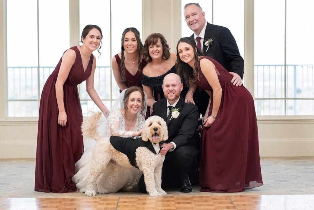 Chuck Stravin (standing, upper right) and wife Liz (kneeling, in black) celebrate the big day with daughters MaryBeth, Meghan, and Colleen (in red, left to right), daughter and son-in-law Kayla and Jimmy McMahon (center), and family goldendoodle Quinn Stravin.