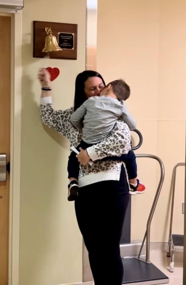 Andrea, helped by son JJ, 2, rings the bell after her last of 19 radiation treatments, Nov. 2023.