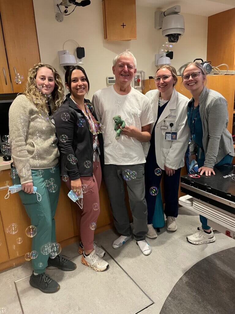 Combes, center, with “Monty,” a good luck charm and conversation starter who travels everywhere with Combes, after the end of radiation treatment. The Dana-Farber team supplied the bubble machine. 